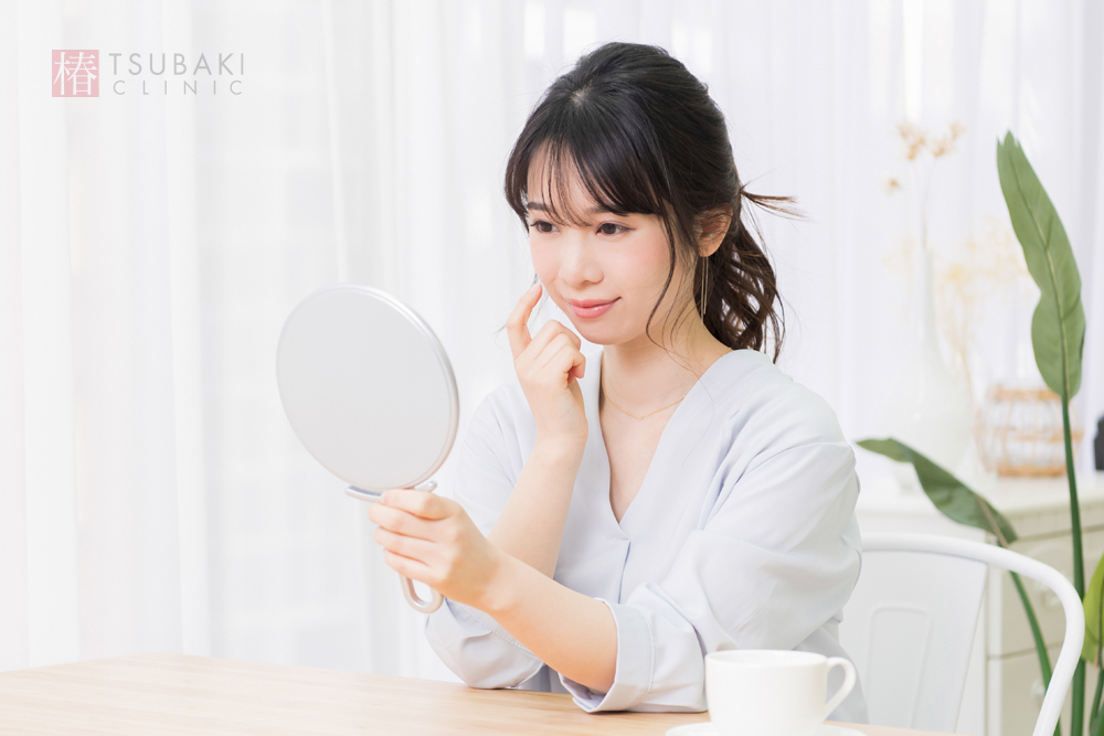 鏡を見ながら頬など顔の部位の肌状態を確認する女性のイメージ写真