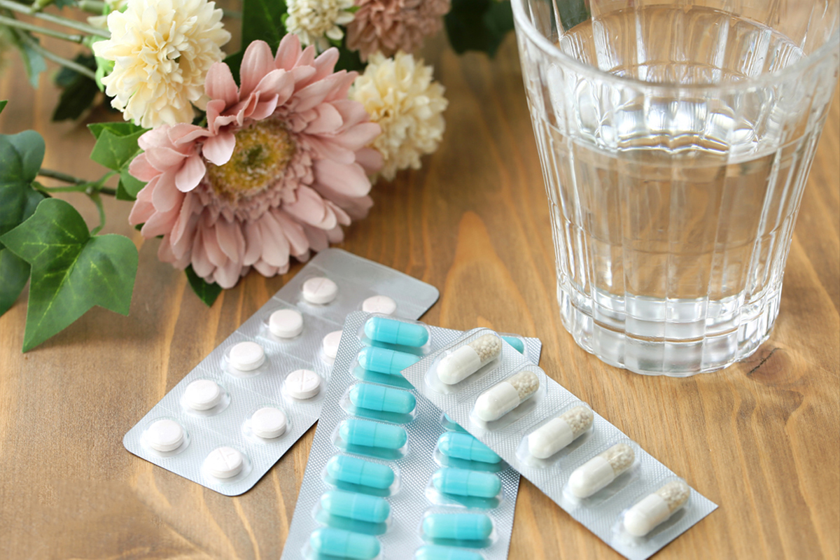 木目調のテーブルの上に造花と水の入った透明のコップ、薬剤のシートが3枚置かれている風景。