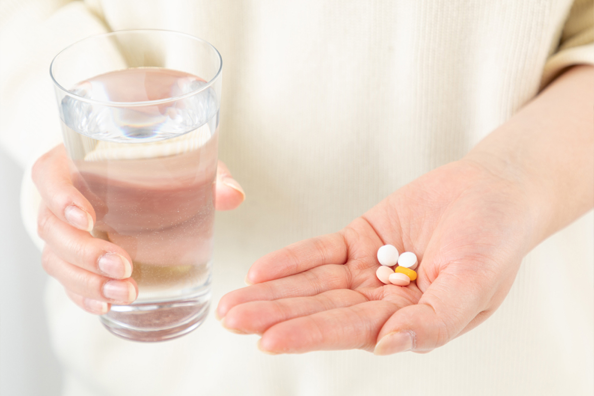 白い服を着た人物の手の中に複数の薬剤があり、反対の手には水の入ったコップを持っている手元のアップの写真。
