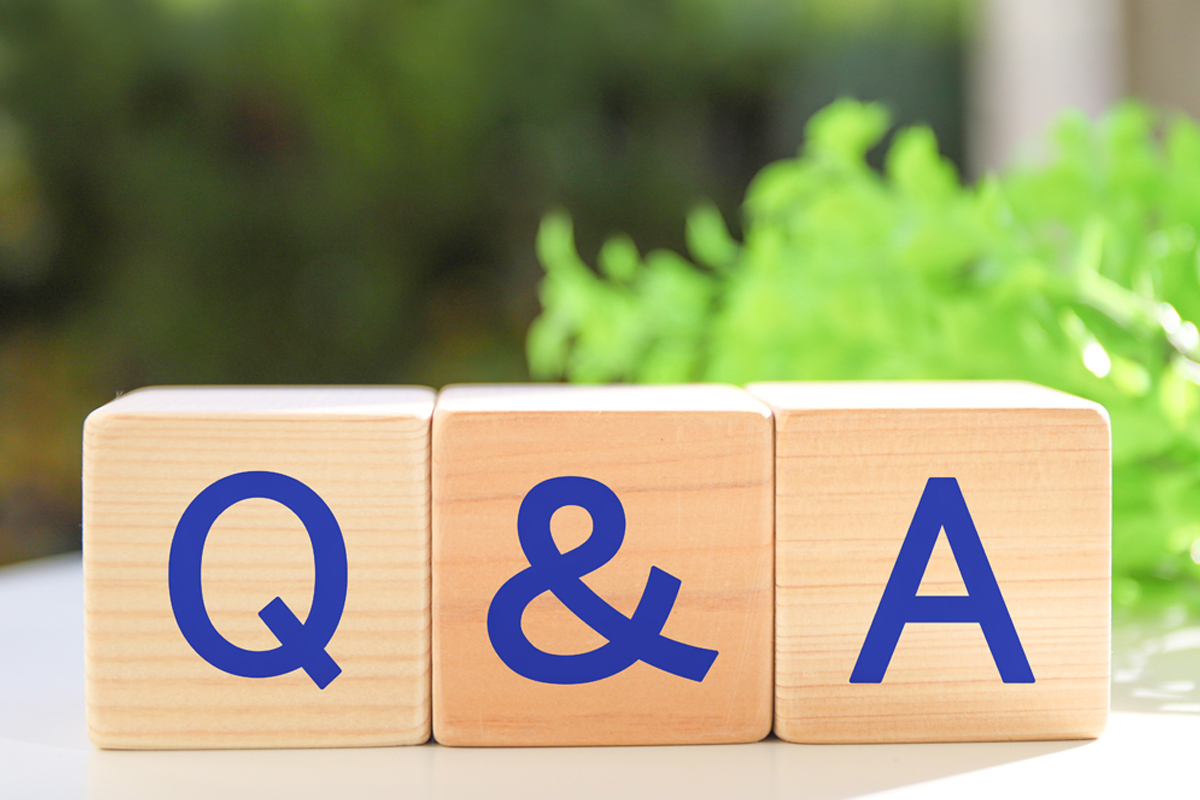 白いテーブルの上に、「Q」「&」「A」と書かれた3つの木製ブロックが横に並んでいます。背景には緑の植物がぼんやりと見えます。