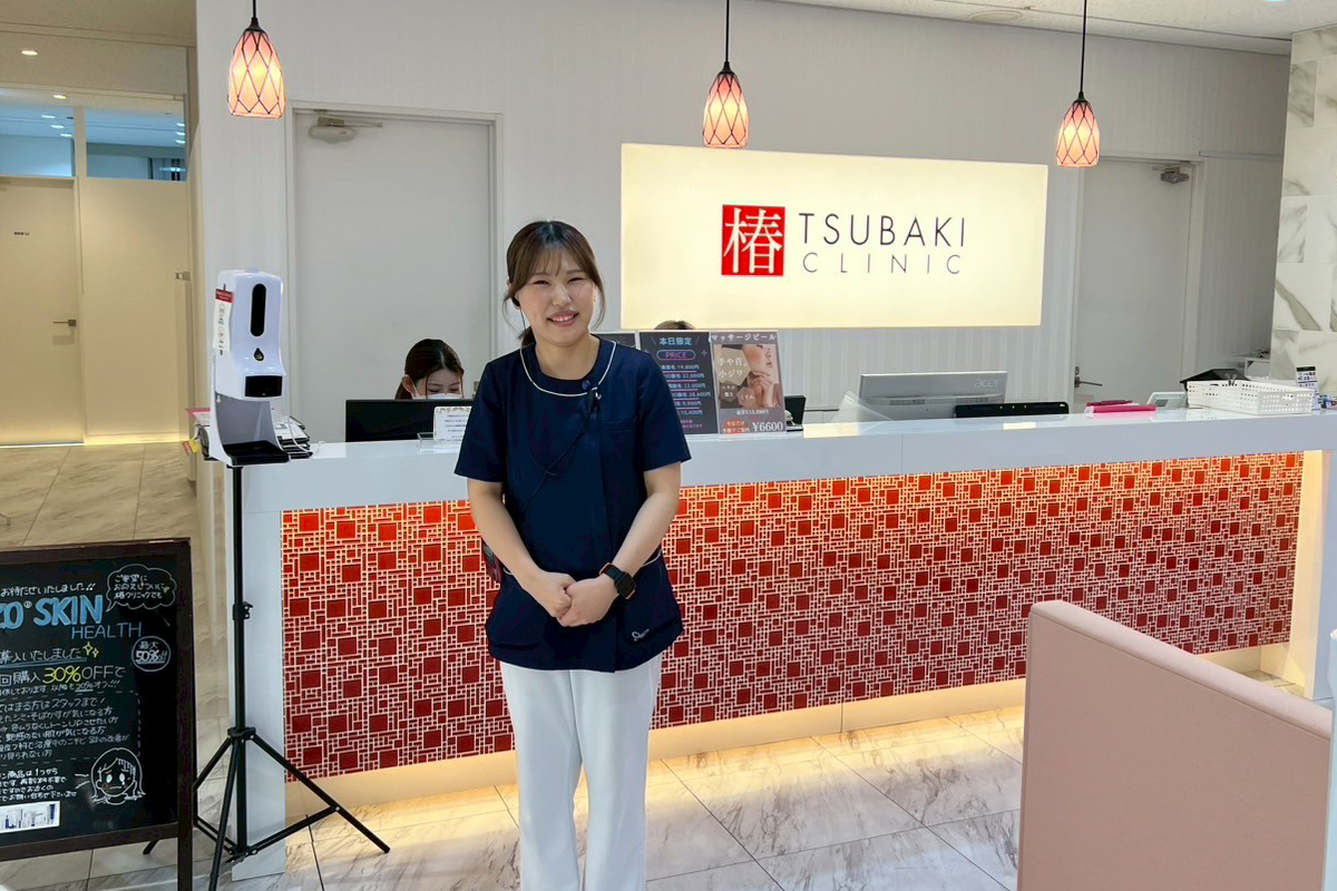 椿クリニックの受付カウンター前で、ネイビーの制服を着たスタッフが笑顔で立っている院内の写真です。
